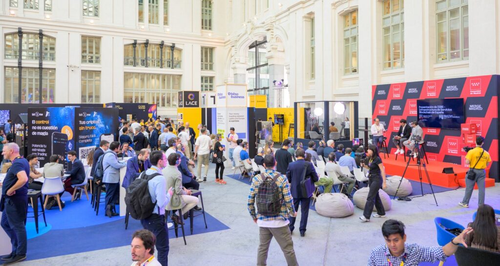 Asistentes recorren stands y siguen un panel en el escenario de MERGE Madrid