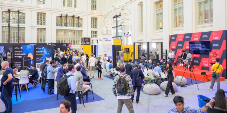 Asistentes recorren stands y siguen un panel en el escenario de MERGE Madrid