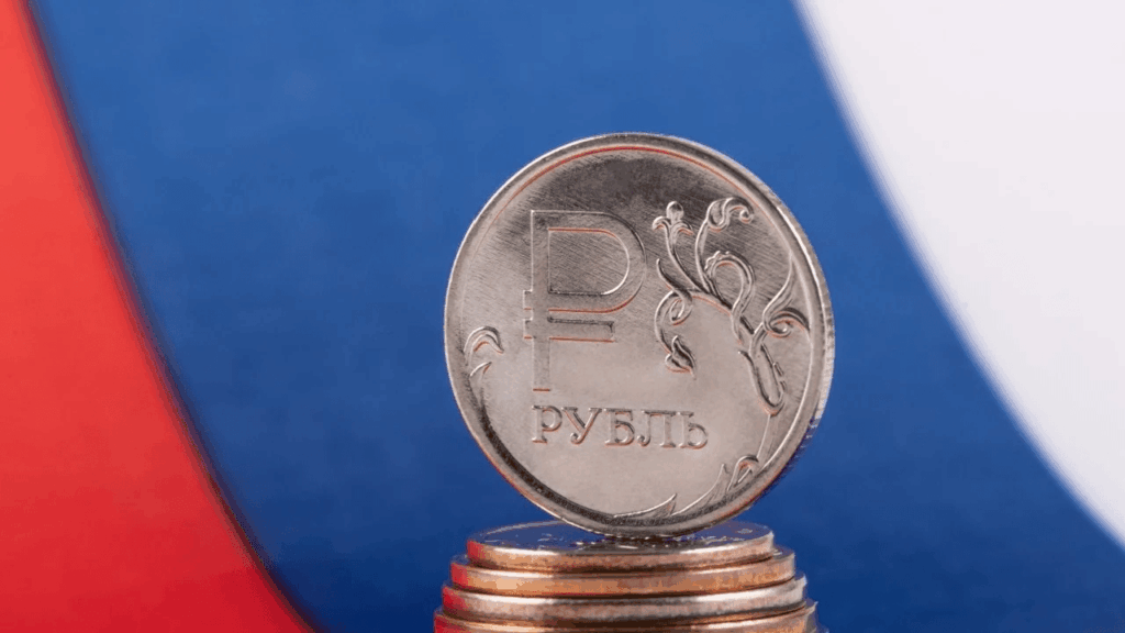Una moneda de rublo de Rusia y detrás la bandera de Rusia