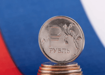 Una moneda de rublo de Rusia y detrás la bandera de Rusia