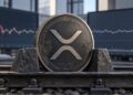 Una moneda física de XRP agarrada por dos bloques de pierdra sobre un escritorio.