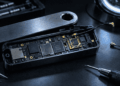 Hardware wallet abierta sobre una mesa, con un módulo espía soldado a la placa y una antena conectada.