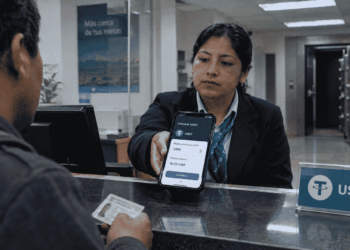 Un cajero bancario extiende un teléfono con la interfaz de compra de USDT a un cliente. Al fondo, una bóveda abierta y vacía. Ilustración: CriptoNoticias.