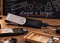Primer plano: hardware wallet Ledger. Fondo: pizarra donde se lee "ataque a ledger"