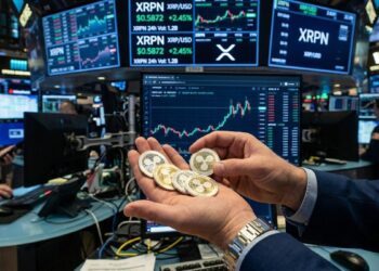 Mano sosteniendo monedas de XRP frente a pantallas bursátiles con el ticker XRPN.