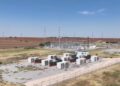 instalación industrial de infraestructura de energía y cómputo, ubicada en una vasta llanura árida bajo un cielo azul despejado y brillante.
