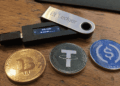 Dispositivo ledger junto a monedas de bitcoin, usdt y usdc.