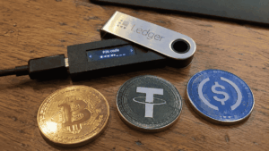 Dispositivo ledger junto a monedas de bitcoin, usdt y usdc.