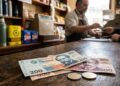 Billetes y monedas de pesos uruguayos sobre el mostrador de madera de un comercio local en Uruguay.