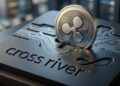 Moneda física con el símbolo de Ripple siendo insertada en una plataforma tecnológica con el logo grabado de Cross River.