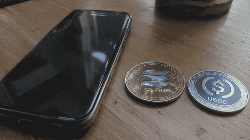 Un teléfono Samsung, una moneda de Solana y una moneda de USDC sobre una mesa.