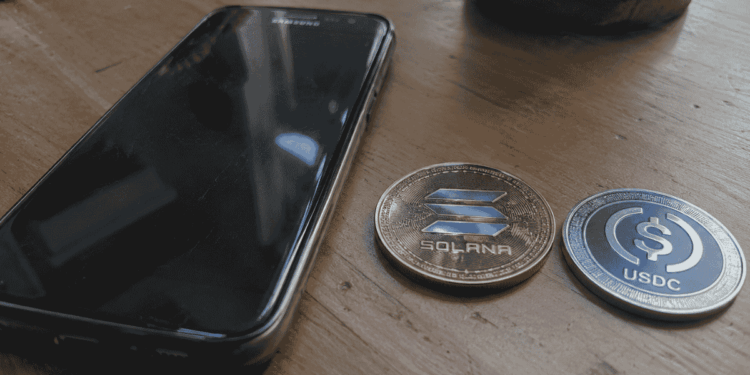 Un teléfono Samsung, una moneda de Solana y una moneda de USDC sobre una mesa.